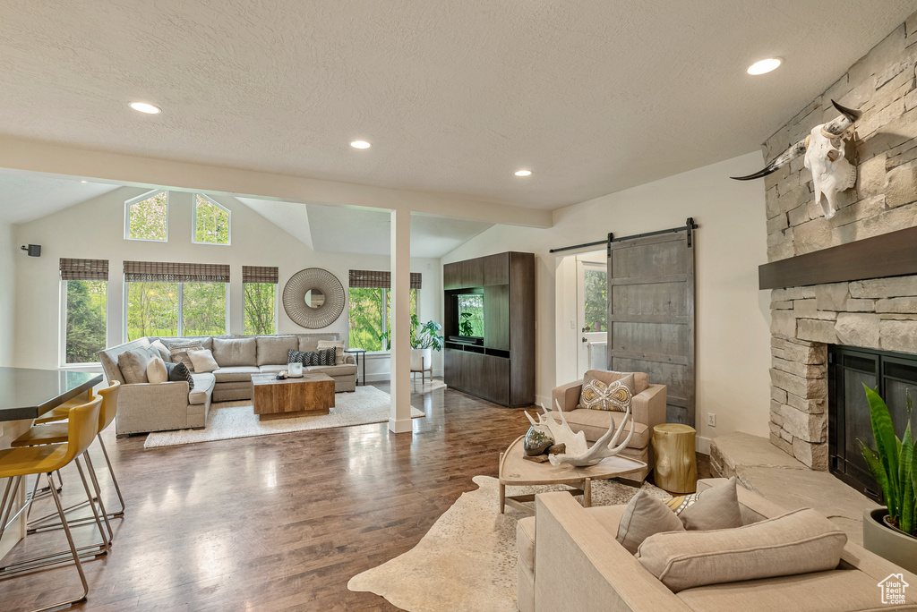 Living room featuring lofted ceiling, a barn door, wood finished floors, a fireplace, and recessed lighting