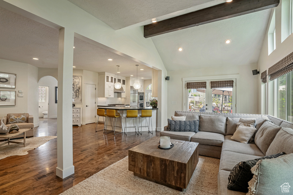 Living room with arched walkways, beam ceiling, dark wood-type flooring, recessed lighting, and a textured ceiling
