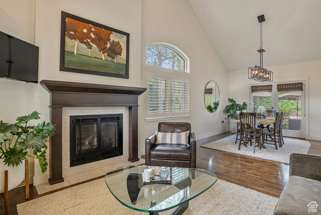 Living room with high vaulted ceiling, a tile fireplace, wood finished floors, baseboards, and a chandelier