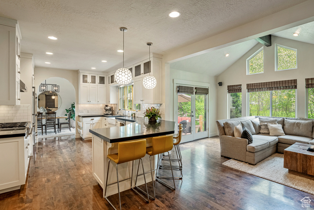Kitchen featuring dark countertops, open floor plan, glass insert cabinets, a peninsula, and decorative backsplash