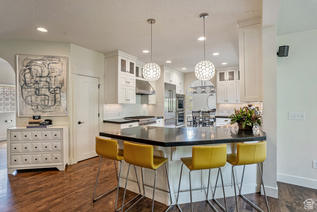 Kitchen with under cabinet range hood, dark countertops, a breakfast bar area, decorative backsplash, and white cabinetry