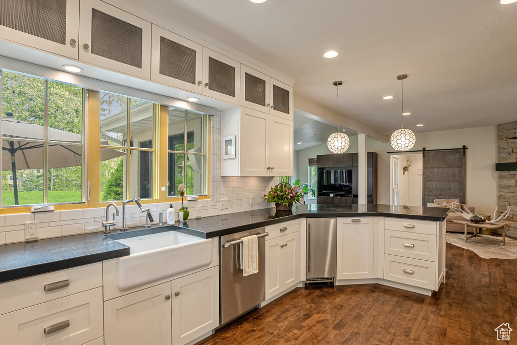 Kitchen with stainless steel dishwasher, a barn door, open floor plan, decorative backsplash, and dark wood-type flooring
