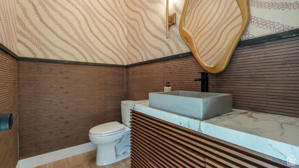 Bathroom featuring wallpapered walls, toilet, wood finished floors, vanity, and wainscoting