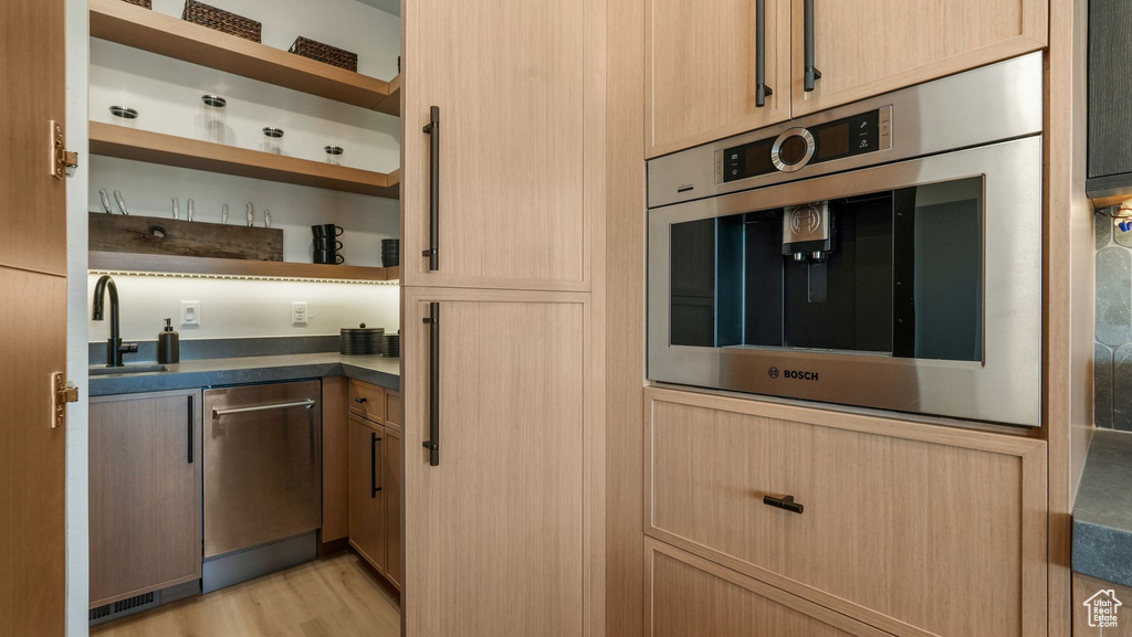 Kitchen featuring dishwasher, open shelves, a sink, dark countertops, and light wood finished floors