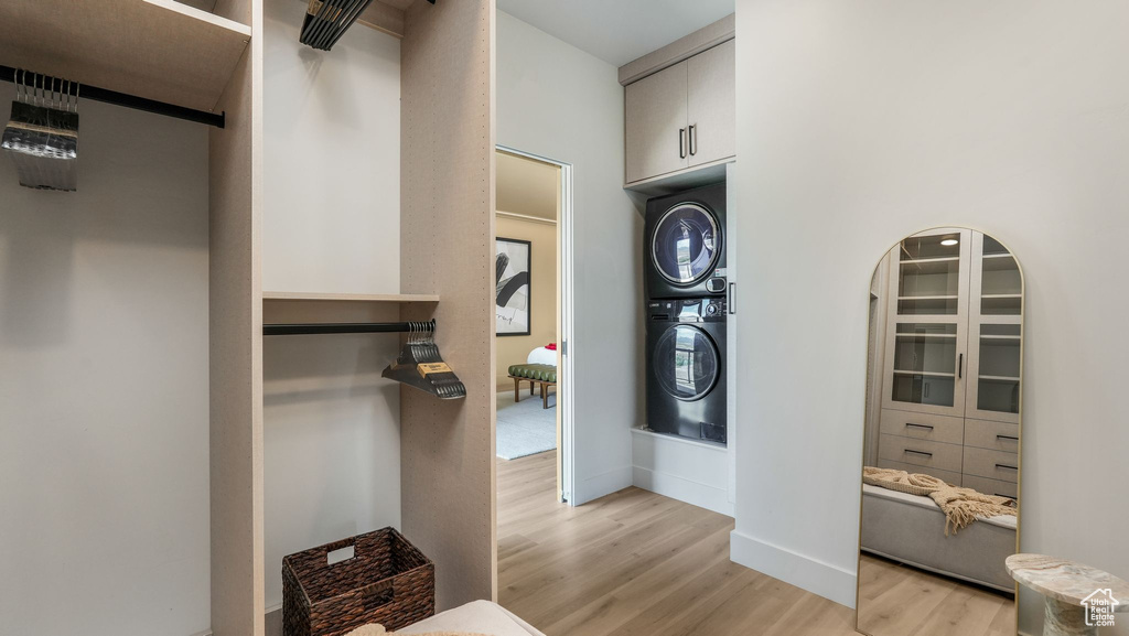 Washroom featuring stacked washing machine and dryer, light wood-style floors, and baseboards