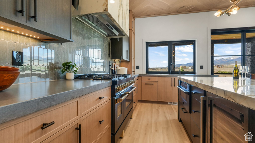 Kitchen with double oven range, beverage cooler, custom range hood, and light brown cabinets