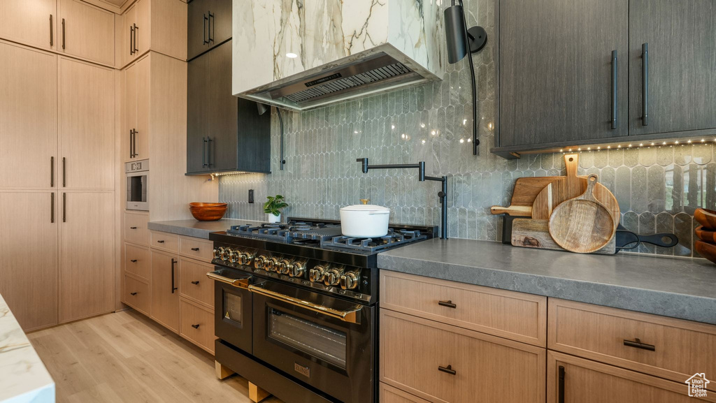 Kitchen featuring range with two ovens, exhaust hood, backsplash, light wood-type flooring, and dark countertops