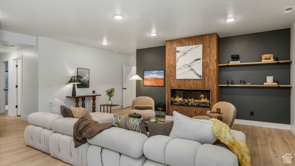 Living room with wood finished floors, a large fireplace, baseboards, and recessed lighting
