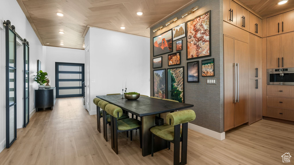 Dining space with light wood finished floors, a barn door, baseboards, and recessed lighting