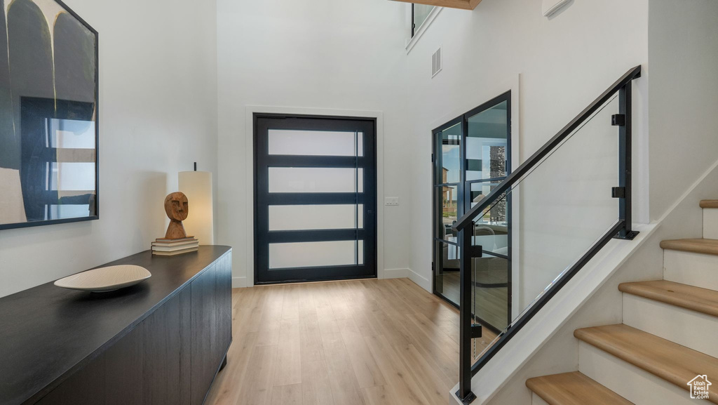 Foyer entrance with stairway, light wood finished floors, baseboards, and a high ceiling
