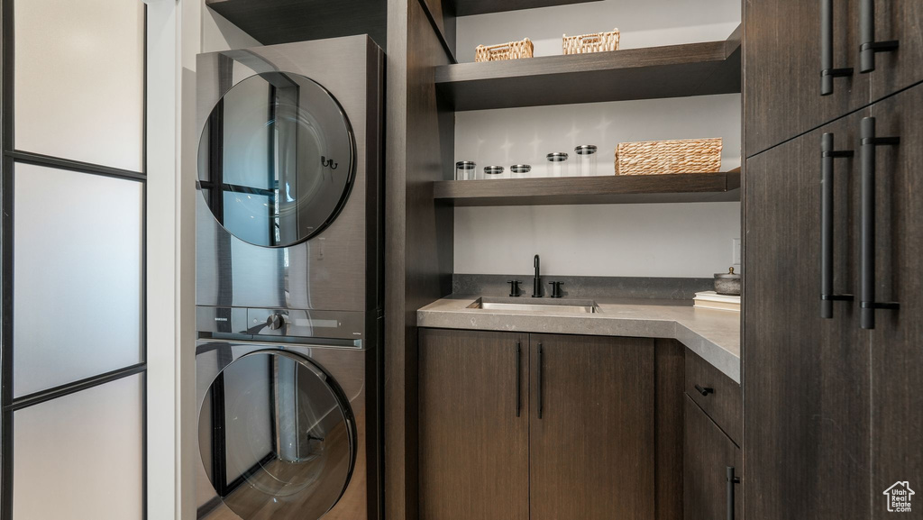 Laundry room featuring stacked washing machine and dryer, cabinet space, and wet bar