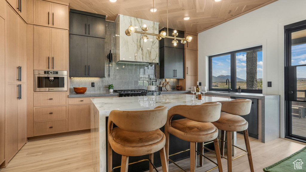 Kitchen featuring decorative backsplash, light wood-style floors, light stone counters, dishwasher, and a kitchen bar