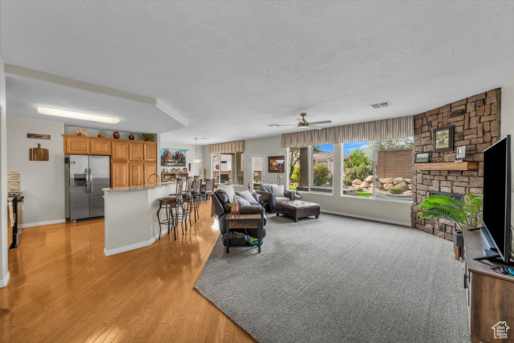 Living area featuring a textured ceiling, light wood finished floors, a ceiling fan, and baseboards