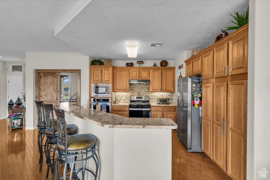 Kitchen featuring appliances with stainless steel finishes, under cabinet range hood, a breakfast bar, light wood-type flooring, and a textured ceiling