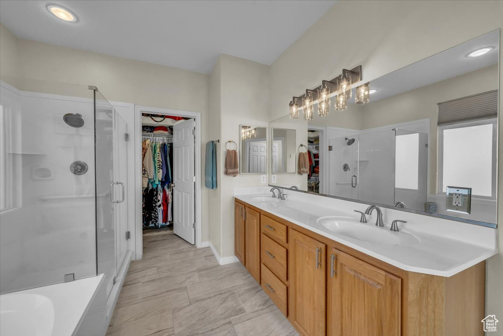 Full bathroom with a walk in closet, a stall shower, double vanity, baseboards, and a chandelier