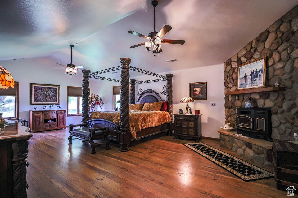 Bedroom featuring vaulted ceiling, a wood stove, multiple windows, and hardwood / wood-style flooring
