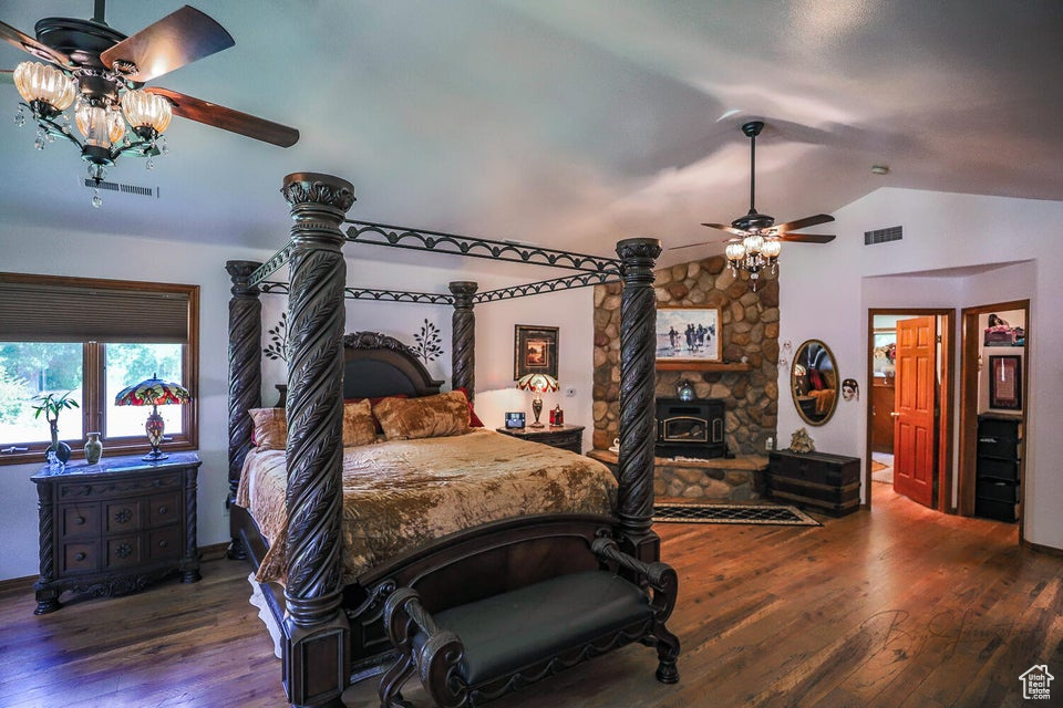 Bedroom with lofted ceiling, wood finished floors, a wood stove, and ceiling fan