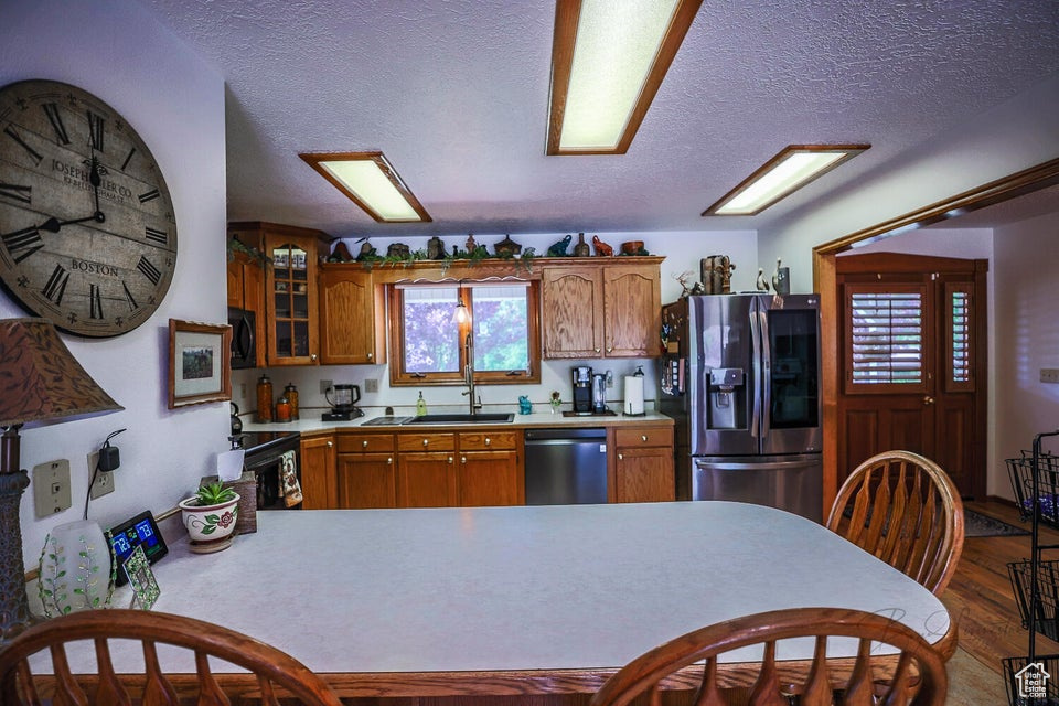 Kitchen featuring black appliances, brown cabinets, a textured ceiling, glass insert cabinets, and light countertops