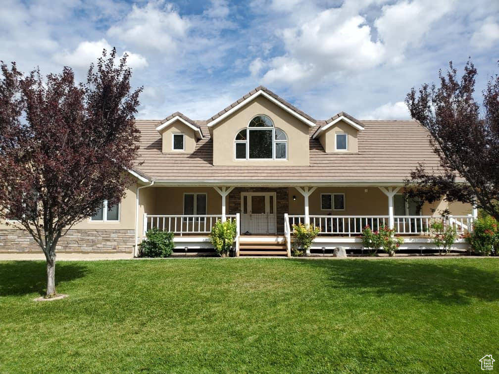Farmhouse inspired home with stucco siding, a front yard, a tile roof, covered porch, and stone siding