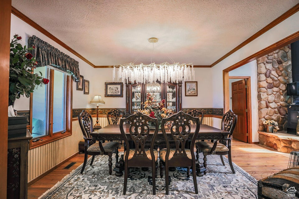 Dining space featuring a chandelier, hardwood / wood-style floors, a wainscoted wall, a textured ceiling, and ornamental molding