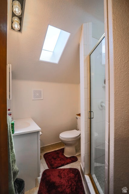 Bathroom featuring a skylight, toilet, vaulted ceiling, a stall shower, and vanity
