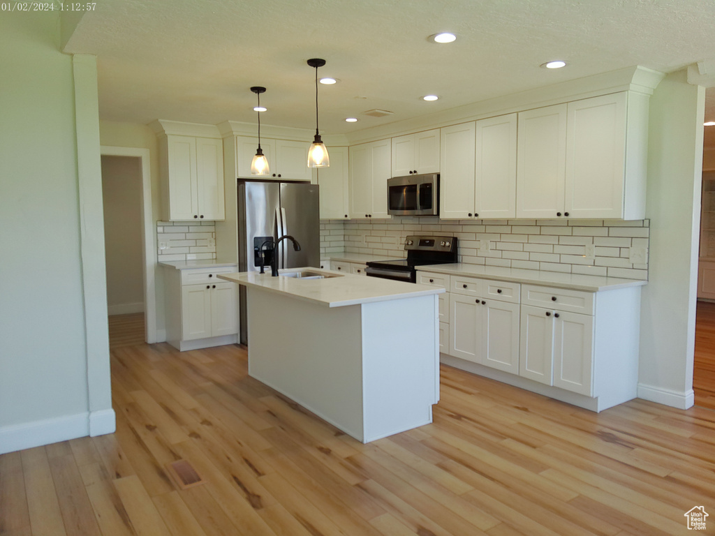 Kitchen with stainless steel appliances, baseboards, light wood-style flooring, decorative backsplash, and white cabinetry