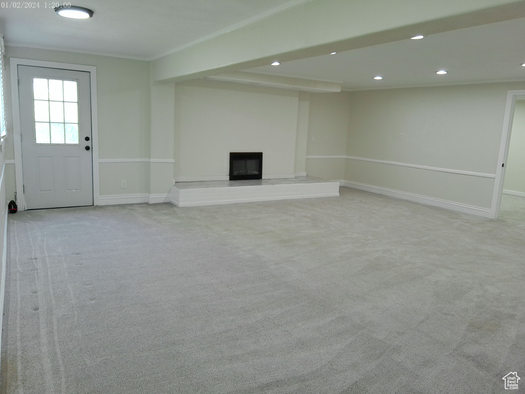 Below grade area with light colored carpet, recessed lighting, a fireplace with raised hearth, baseboards, and crown molding