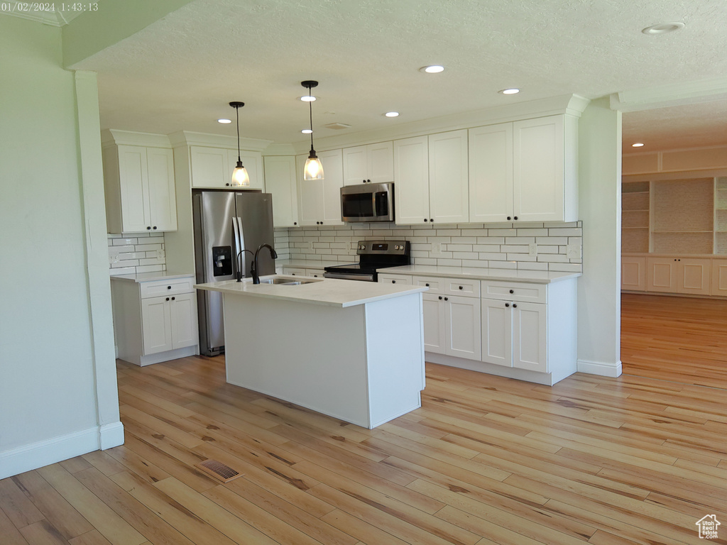Kitchen with stainless steel appliances, a sink, light wood finished floors, white cabinets, and recessed lighting