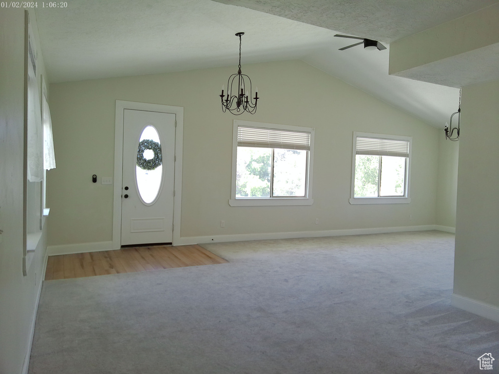Foyer entrance with light colored carpet, a chandelier, lofted ceiling, and baseboards