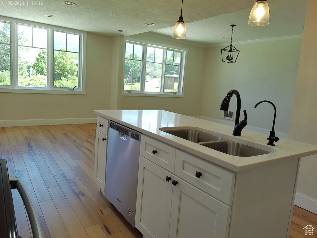 Kitchen featuring stainless steel dishwasher, a sink, decorative light fixtures, white cabinetry, and light countertops