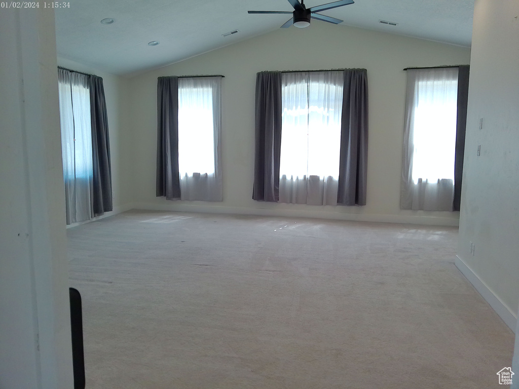 Carpeted empty room with a ceiling fan, vaulted ceiling, healthy amount of natural light, and baseboards