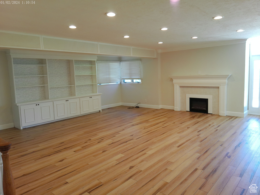 Unfurnished living room featuring recessed lighting, light wood-type flooring, a fireplace, baseboards, and crown molding