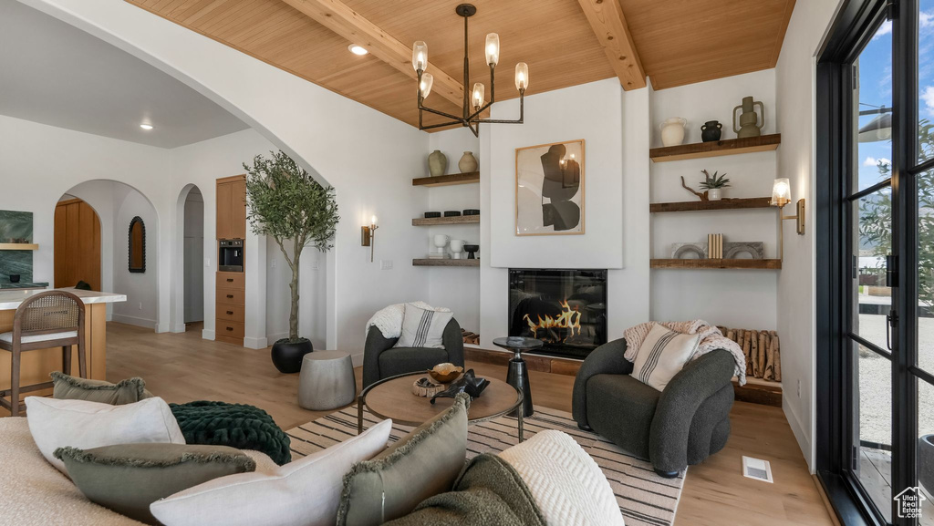 Living room featuring arched walkways, wooden ceiling, light wood-style flooring, a glass covered fireplace, and built in features