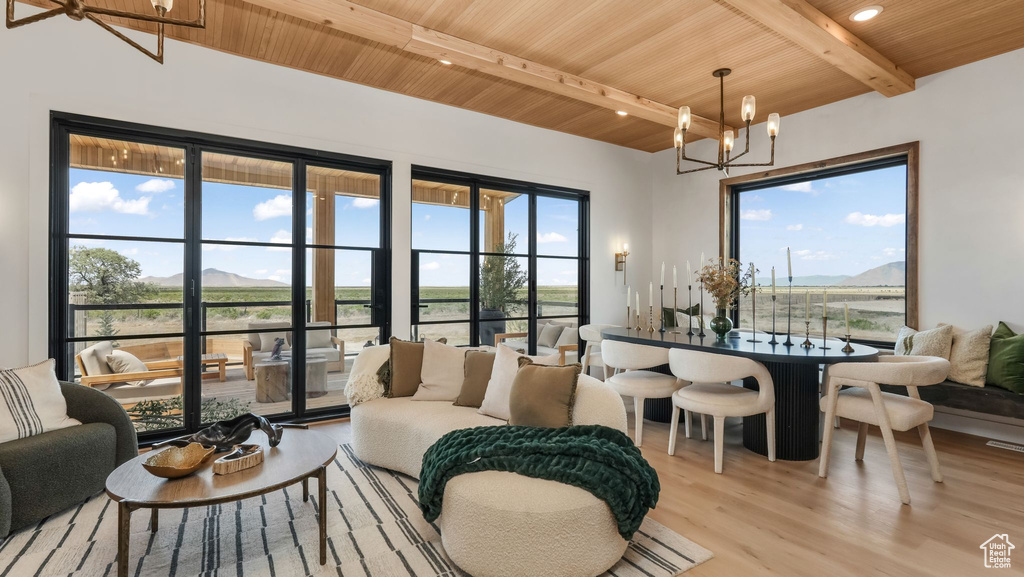 Living room with a chandelier, wooden ceiling with exposed beams, light wood-type flooring, a mountain view, and healthy amount of natural light