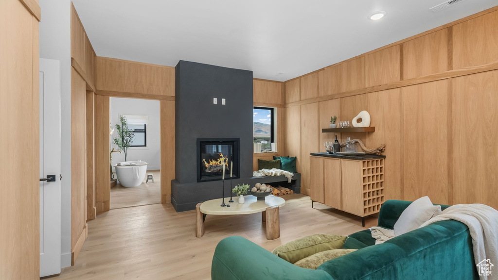 Living room with light wood-type flooring, a multi sided fireplace, and wood walls