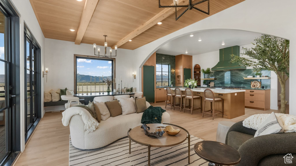 Living room featuring wooden ceiling with exposed beams, arched walkways, light wood finished floors, a chandelier, and recessed lighting