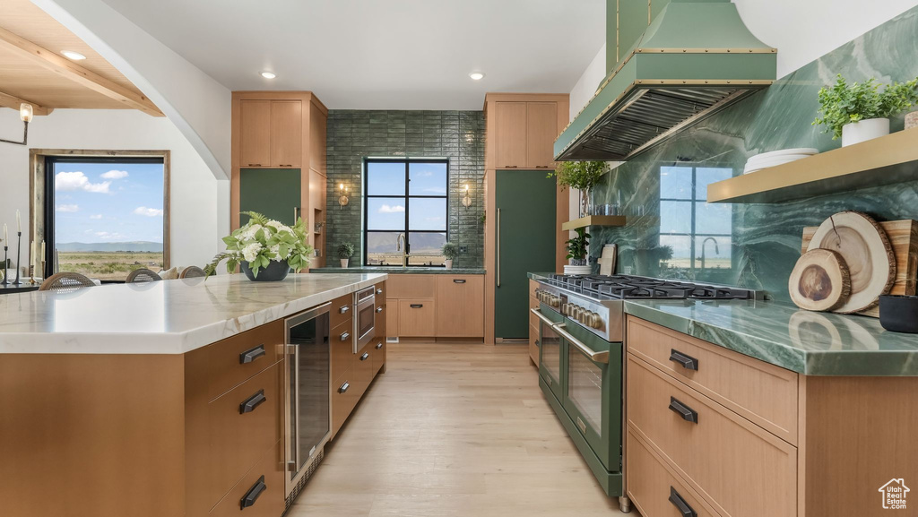 Kitchen with stainless steel appliances, wine cooler, exhaust hood, light wood-style flooring, and backsplash