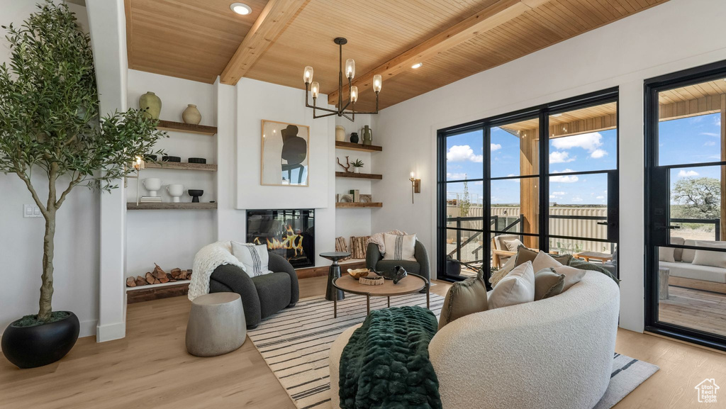 Living room featuring wood ceiling with exposed beams, wood finished floors, built in shelves, a glass covered fireplace, and a chandelier