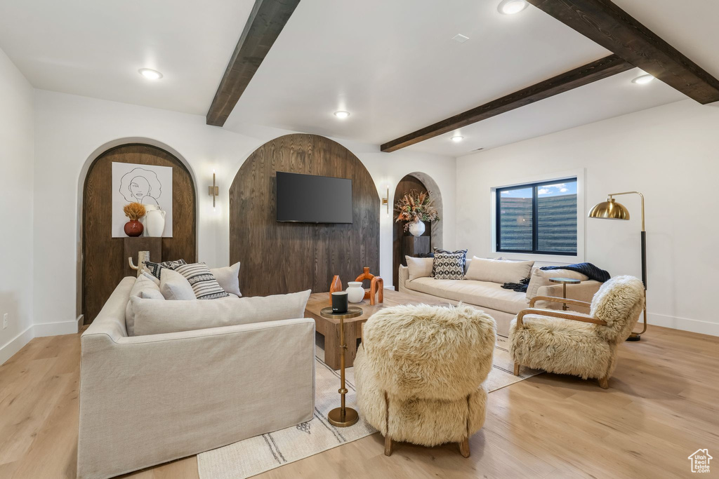 Living area featuring arched walkways, beamed ceiling, light wood finished floors, baseboards, and recessed lighting