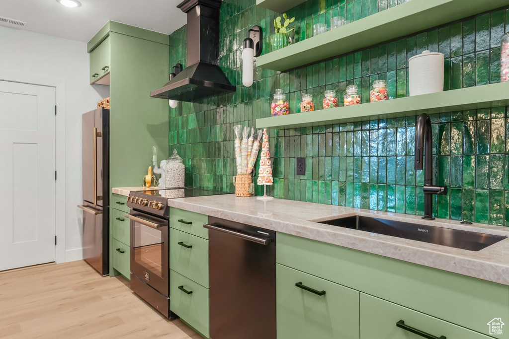 Kitchen with green cabinetry, a sink, wall chimney range hood, electric stove, and freestanding refrigerator