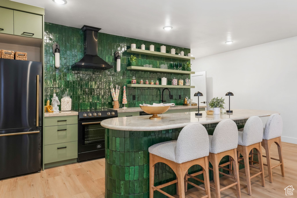 Indoor bar with black appliances, wall chimney exhaust hood, light wood finished floors, decorative backsplash, and recessed lighting