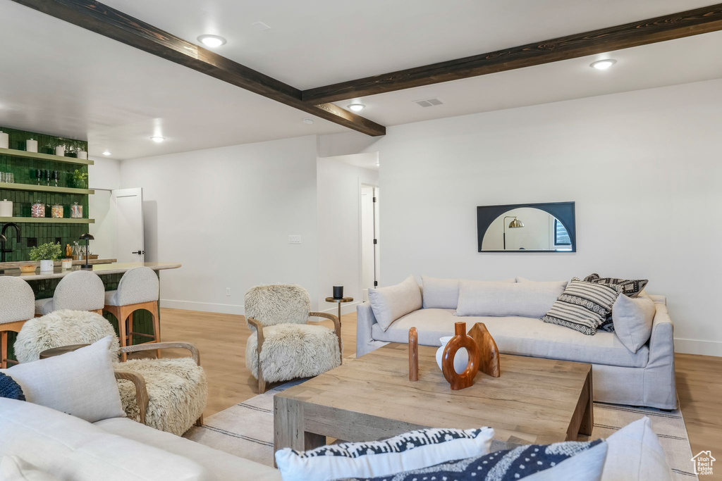 Living room featuring light wood-style floors, wet bar, baseboards, beamed ceiling, and recessed lighting