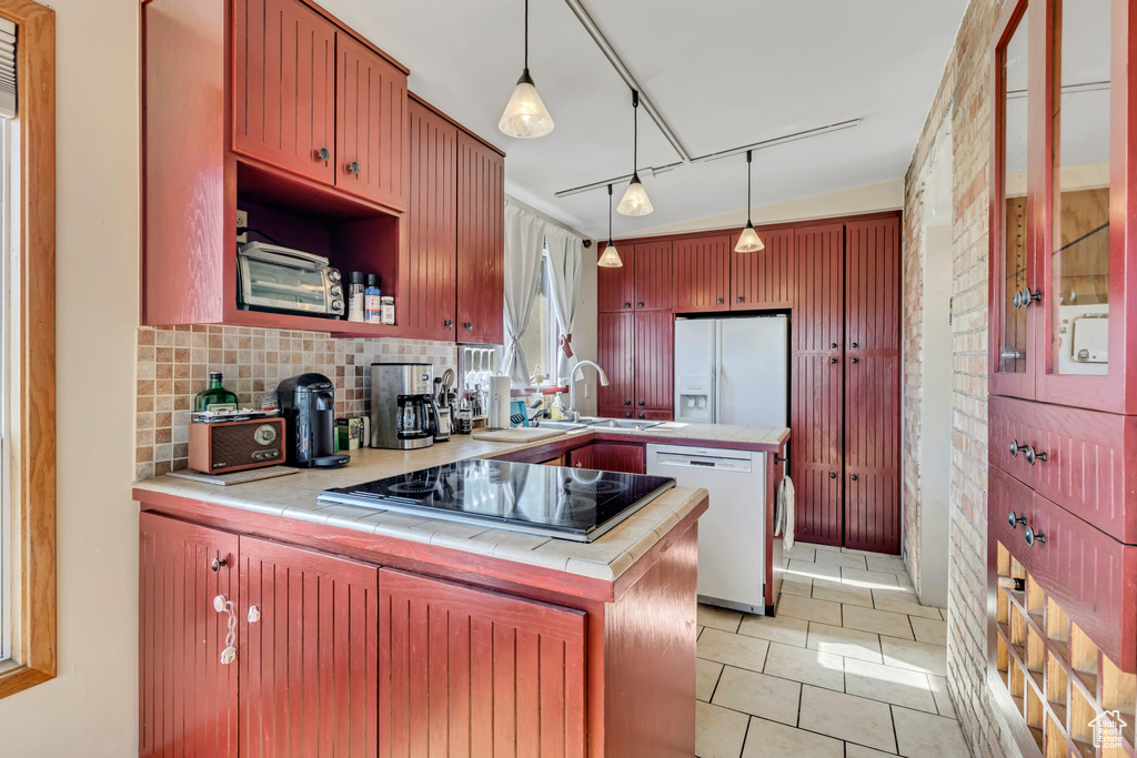 Kitchen with white appliances, a peninsula, decorative backsplash, and tile counters