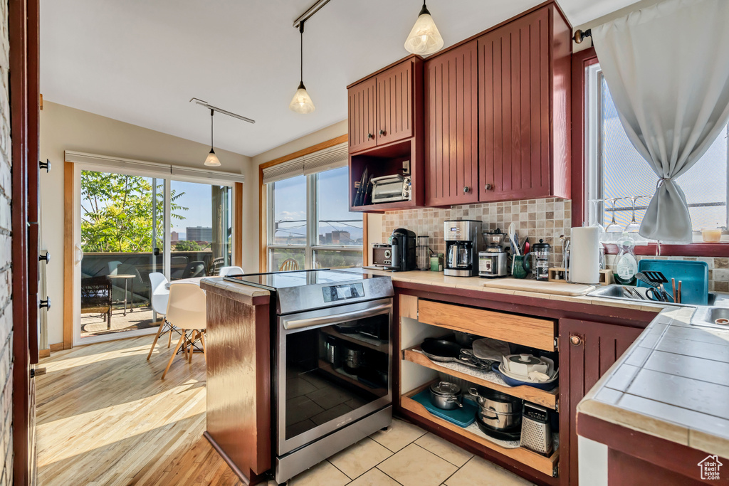 Kitchen with tile countertops, stainless steel range with electric cooktop, vaulted ceiling, tasteful backsplash, and pendant lighting