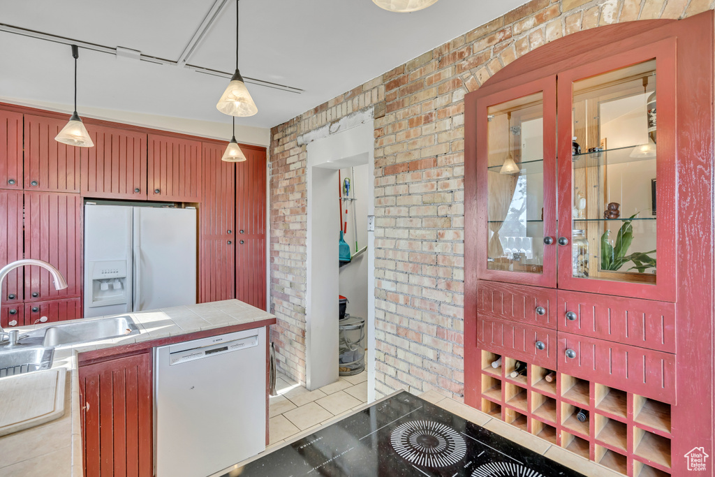 Kitchen featuring dishwasher, white fridge with ice dispenser, brick wall, tile countertops, and light tile patterned floors