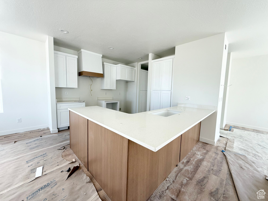 Kitchen with a peninsula, white cabinets, light wood-style floors, light countertops, and a textured ceiling