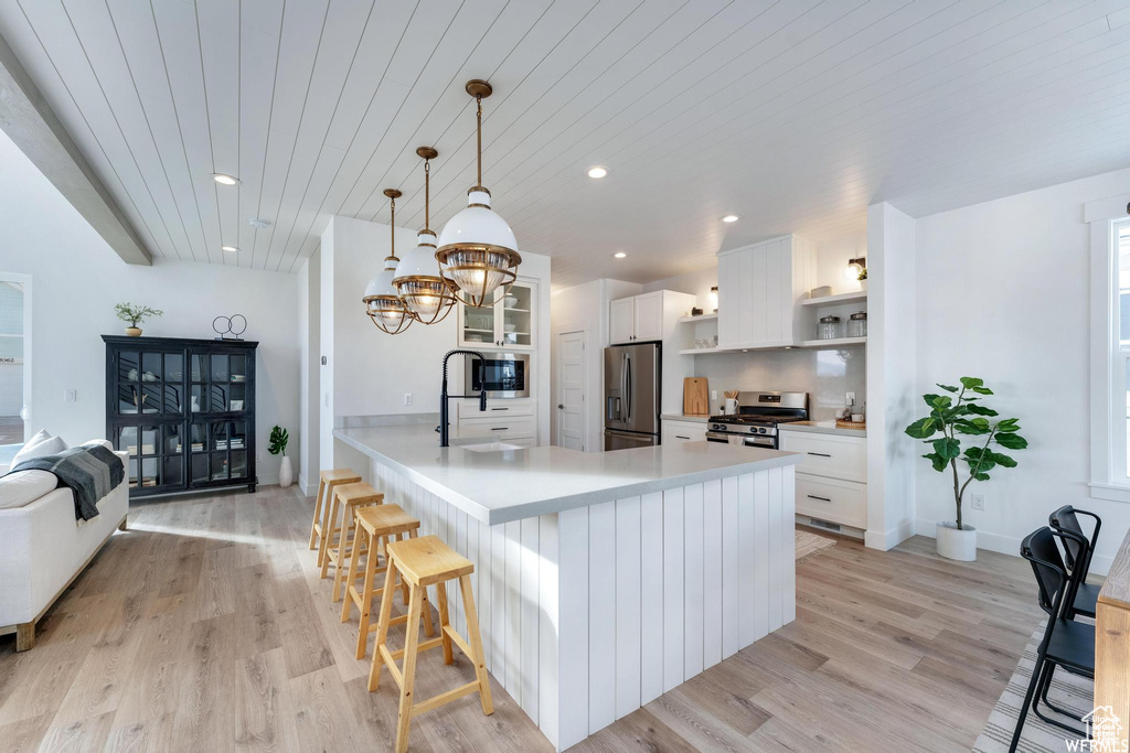 Kitchen with stainless steel appliances, open shelves, white cabinets, light wood-style flooring, and recessed lighting
