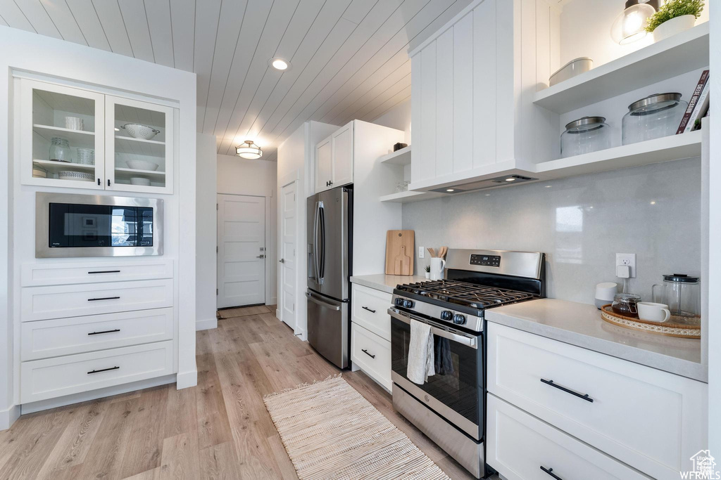 Kitchen with appliances with stainless steel finishes, open shelves, white cabinetry, light countertops, and light wood-style flooring