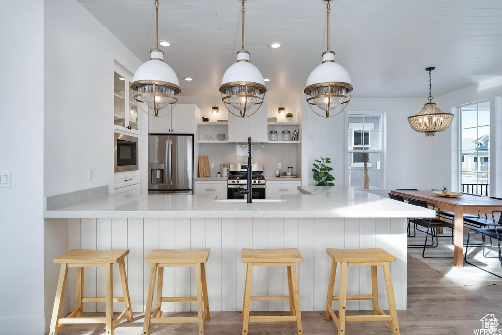 Kitchen featuring appliances with stainless steel finishes, open shelves, a sink, pendant lighting, and white cabinets