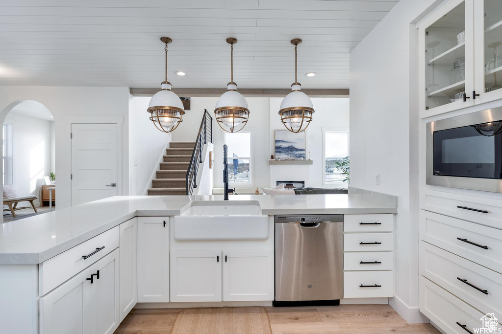 Kitchen featuring stainless steel dishwasher, built in microwave, arched walkways, light countertops, and a sink